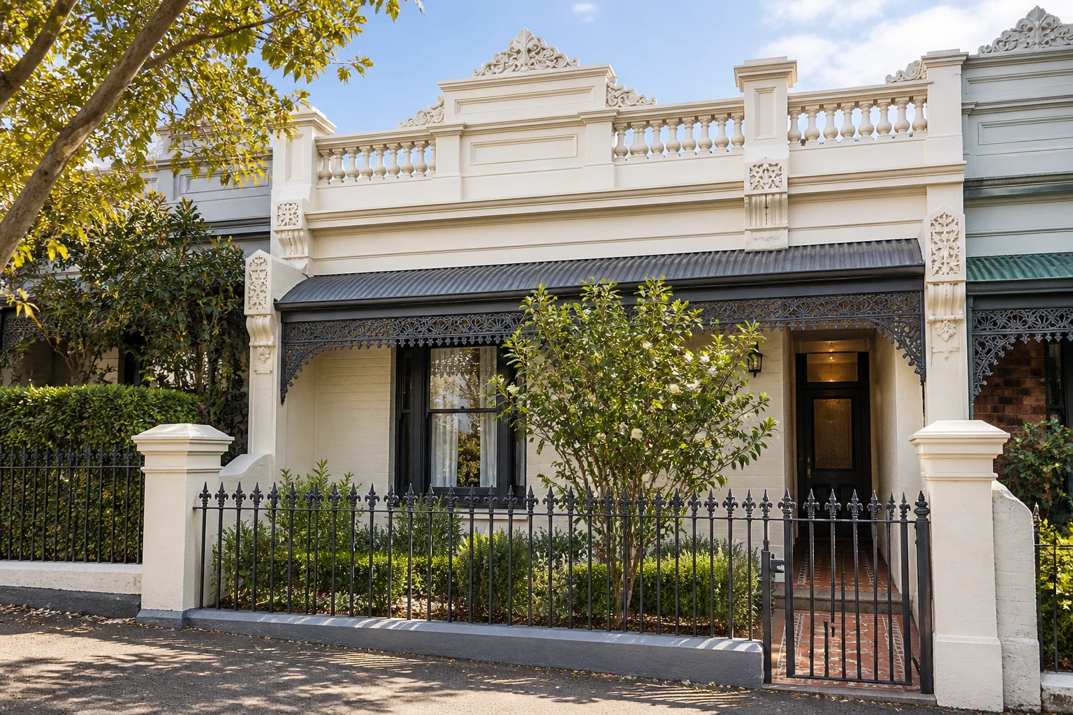 Cream terrace with a foliate parapet crest, dark iron verandah and iron-fenced garden.